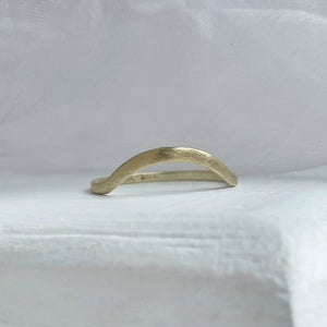 A close-up image of a handcrafted yellow gold wedding band with a high arch and rustic texture. Made with recycled ethical gold and stamped with 10k, 14k, or 18k. Available in a range of sizes.