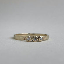 Load image into Gallery viewer, Image of a thin 10k, 14kt, or 18kt yellow gold wedding band with three 1.5mm round Canadian diamonds. The diamonds are SI2-SI3 melee analyzed by GIA. The band is ethically sourced and made from recycled gold.