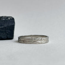 Load image into Gallery viewer, A close-up photo of a white gold wedding band with a geometric-inspired design, handcrafted using ethically sourced and recycled gold. The band measures 4mm wide and 1mm thick and is available in various sizes