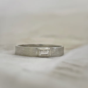 Solitaire baguette engagement ring with rustic texture, handcrafted in eco-friendly 10k white gold and ethically sourced white sapphire.