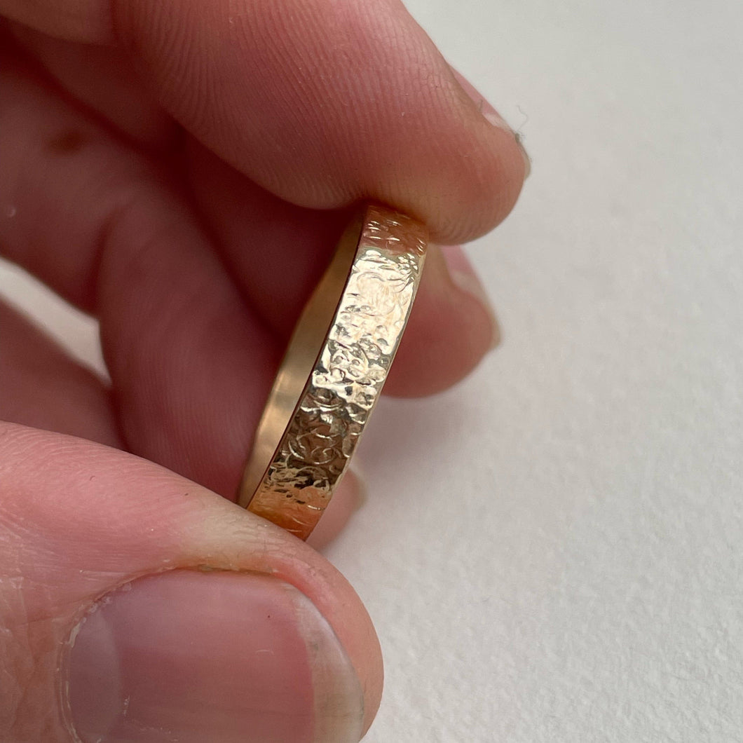 Image of a 4mm hammered finish yellow gold wedding band with a freestyle hammered texture. The band is made with recycled ethical solid 10kt, 14kt, or 18kt yellow gold and is stamped with its karat weight and hallmarked. Available in a range of sizes and made to order, shipping includes tracking within Canada and the United States, and internationally. The ring comes gift-wrapped, making it a special and meaningful present
